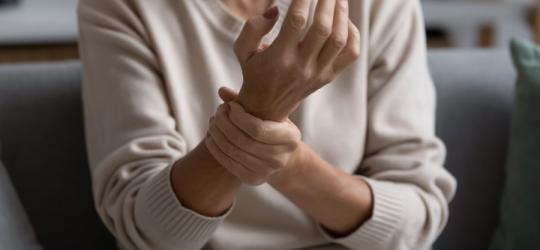 Kobieta trzyma się za rękę, odczuwa ból stawów.