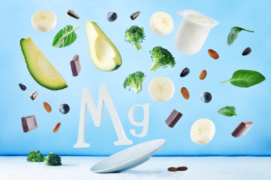 Symbol magnezu Mg i jego źródła - brokuły, plastry banana, jogurt, szpinak, czekolada, orzechy.