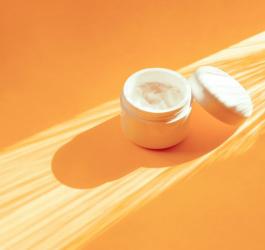 Słoiczek z maścią z witaminą A, leżący na pomarańczowym tle.