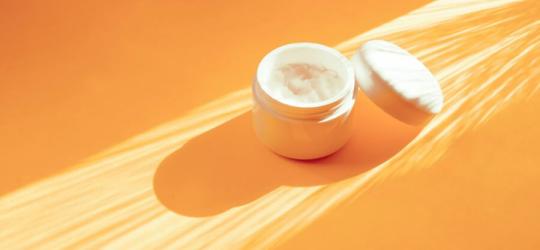 Słoiczek z maścią z witaminą A, leżący na pomarańczowym tle.