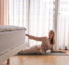 Kobieta wykonuje ćwiczenia rehabilitacyjne na macie obok łóżka.