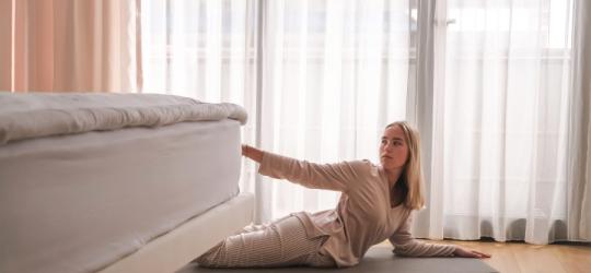 Kobieta wykonuje ćwiczenia rehabilitacyjne na macie obok łóżka.