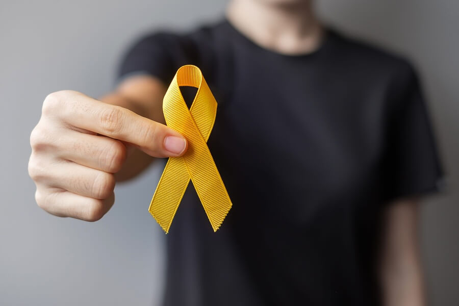 Kobieta trzyma w ręce żółtą wstążkę – symbol świadomości i walki z mięsakiem.
