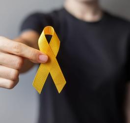 Kobieta trzyma w ręce żółtą wstążkę – symbol świadomości i walki z mięsakiem.
