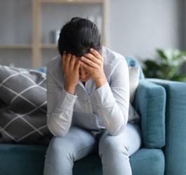 Kobieta siedzi na sofie, trzyma się za głowę. Męczy ją silna migrena.