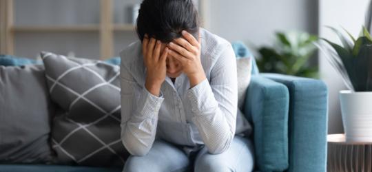 Kobieta siedzi na sofie, trzyma się za głowę. Męczy ją silna migrena.