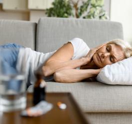 Kobieta leży na kanapie i trzyma się za głowę. Dokucza jej migrena z aurą.