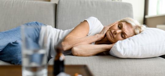 Kobieta leży na kanapie i trzyma się za głowę. Dokucza jej migrena z aurą.