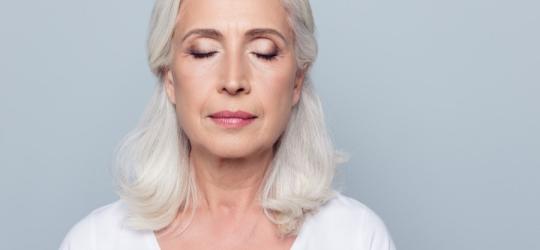 Starsza kobieta przymyka powieki, ma mroczki przed oczami.