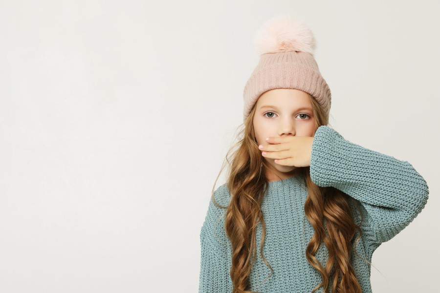 Dziewczynka w czapce zasłania usta dłonią. Nic nie mówi, co wskazuje na mutyzm.