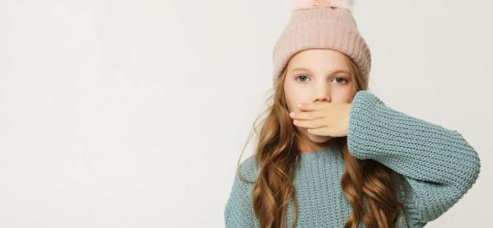 Dziewczynka w czapce zasłania usta dłonią. Nic nie mówi, co wskazuje na mutyzm.
