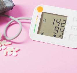 Różowe tło. Naramienny ciśnieniomierz wyświetla wyniki wskazujące na nadciśnienie tętnicze.