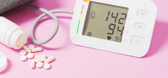 Różowe tło. Naramienny ciśnieniomierz wyświetla wyniki wskazujące na nadciśnienie tętnicze.