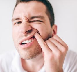 Mężczyzna przegląda się w lustrze, ma nadziąślaka nad zębem.