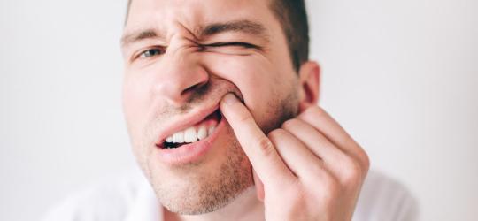 Mężczyzna przegląda się w lustrze, ma nadziąślaka nad zębem.