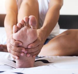Osoba trzyma się dłońmi za stopę, doskwierają jej bolesne nagniotki.