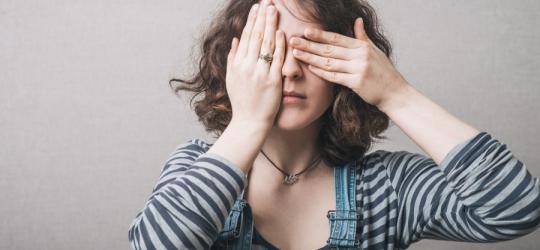 Kobieta zasłania dłońmi oczy, co symbolizuje rozmaite choroby oczu.