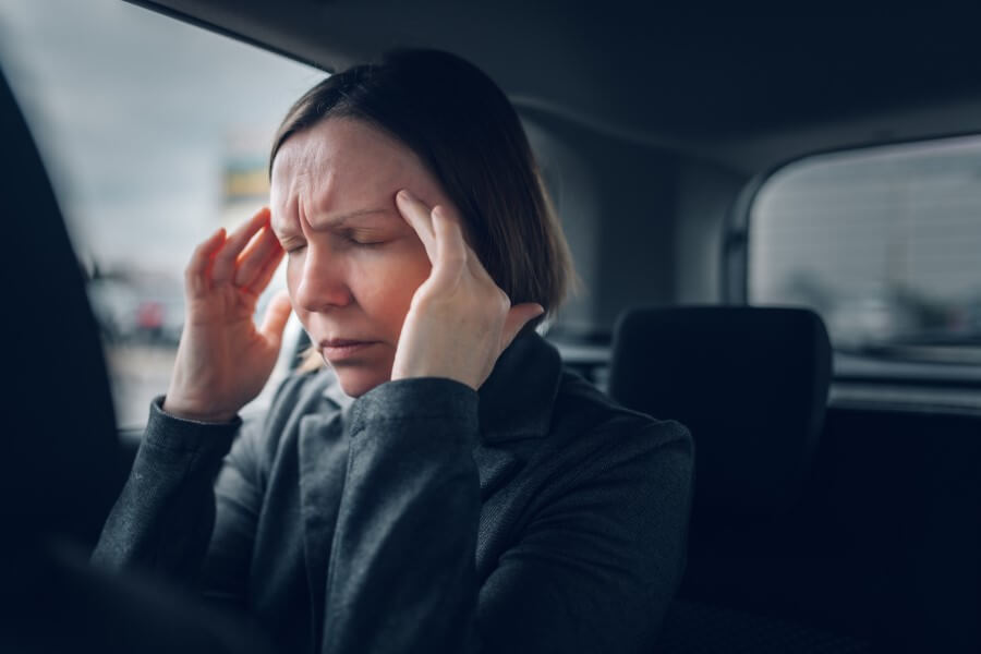 Kobieta siedzi w samochodzie, dokucza jej silny, napięciowy ból głowy.