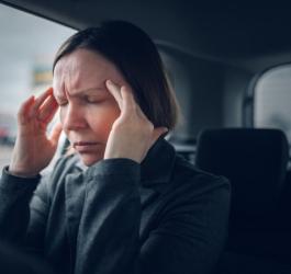 Kobieta siedzi w samochodzie, dokucza jej silny, napięciowy ból głowy.