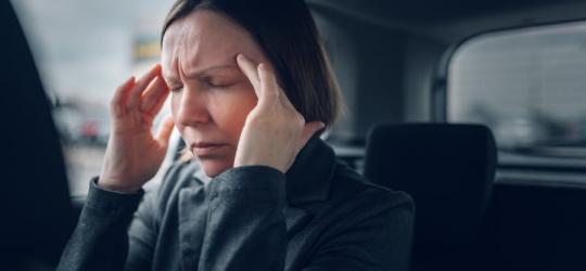 Kobieta siedzi w samochodzie, dokucza jej silny, napięciowy ból głowy.