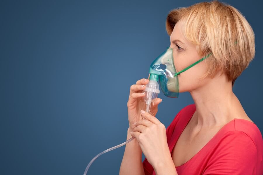 Kobieta używa nebulizatora do podania leku wziewnego.