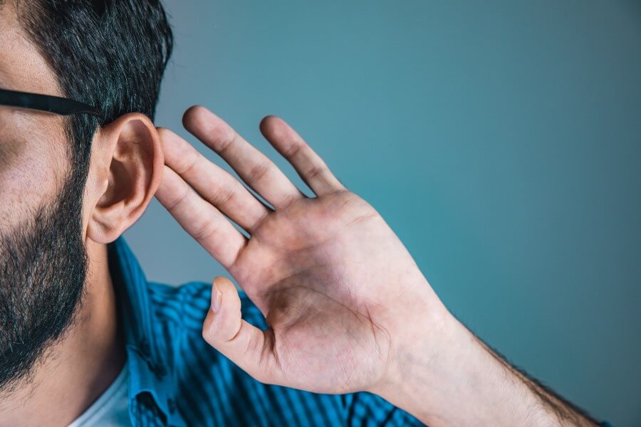 Mężczyzna cierpi na niedosłuch, nadstawia ucha, aby słyszeć lepiej.