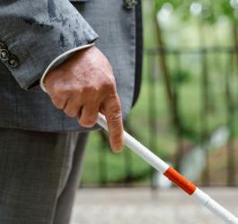 Osoba trzyma w dłoni laskę dla osób niewidomych.