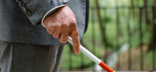 Osoba trzyma w dłoni laskę dla osób niewidomych.