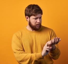 Żółte tło. Brodaty mężczyzna w żółtym swetrze mierzy sobie tętno na nadgarstku, ma niski puls.