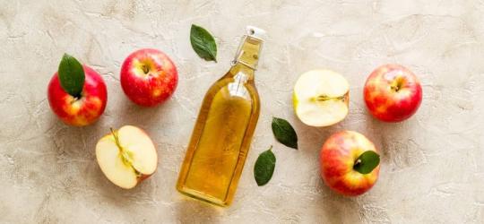 Butelka octu jabłkowego i świeże jabłka na beżowym tle.