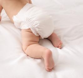 Niemowlę w pieluszce raczkuje po pościeli.