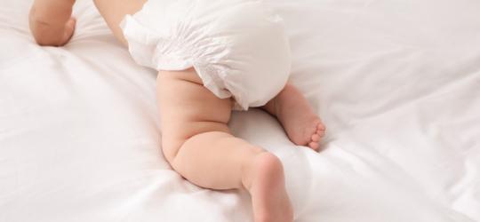 Niemowlę w pieluszce raczkuje po pościeli.