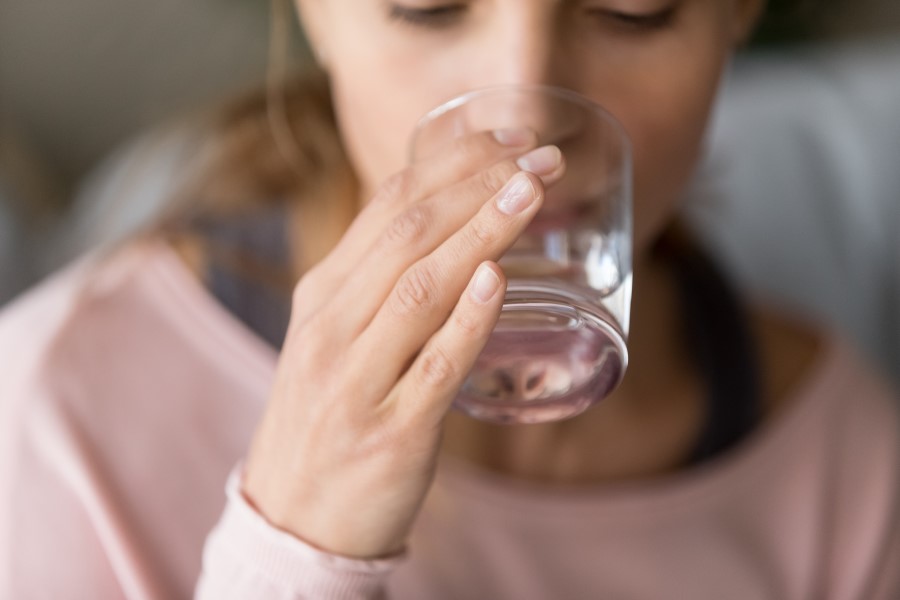 Kobieta pije wodę ze szklanki, aby nie dopuścić do odwodnienia organizmu.