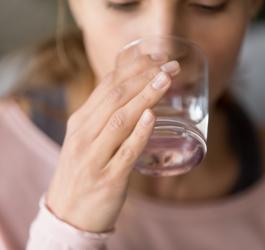 Kobieta pije wodę ze szklanki, aby nie dopuścić do odwodnienia organizmu.