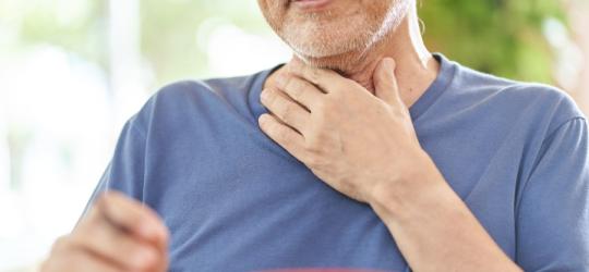 Starszy mężczyzna zmaga się z odynofalgią - odczuwa ból podczas przełykania. Trzyma się za gardło.