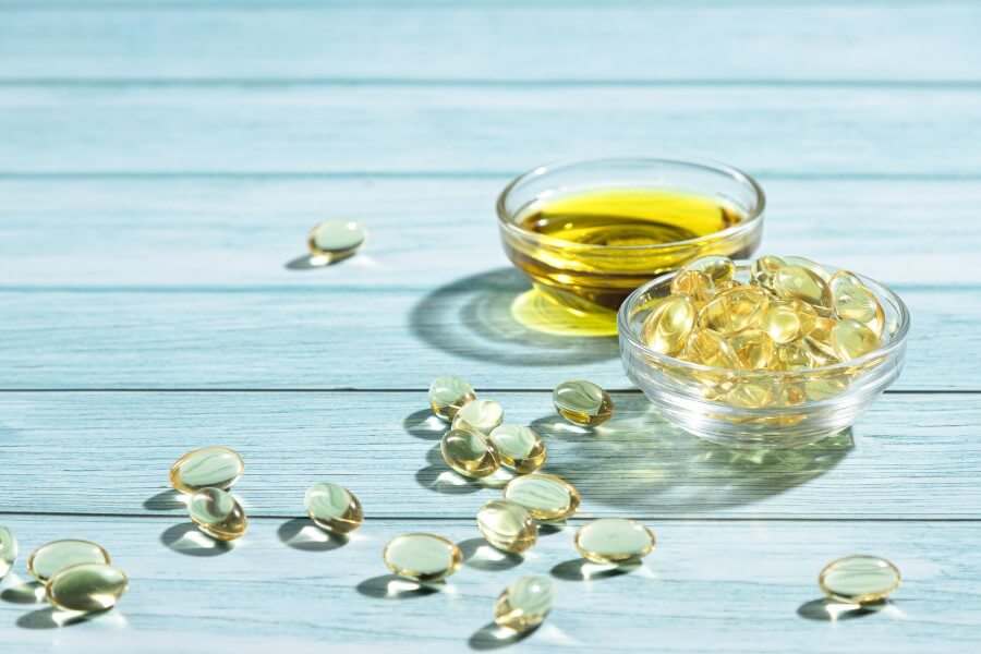 Olej z wiesiołka zamknięty w żelowych kapsułkach oraz w formie płynnej w szklanej miseczce.