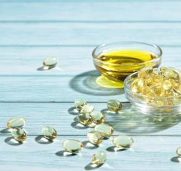 Olej z wiesiołka zamknięty w żelowych kapsułkach oraz w formie płynnej w szklanej miseczce.