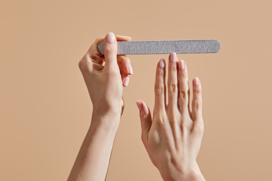 Kobieta piłuje paznokcie przy pomocy papierowego pilniczka.