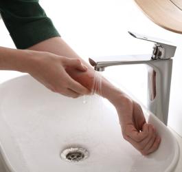 Kobieta schładza przedramię pod strumieniem zimnej wody z kranu po oparzeniu skóry.