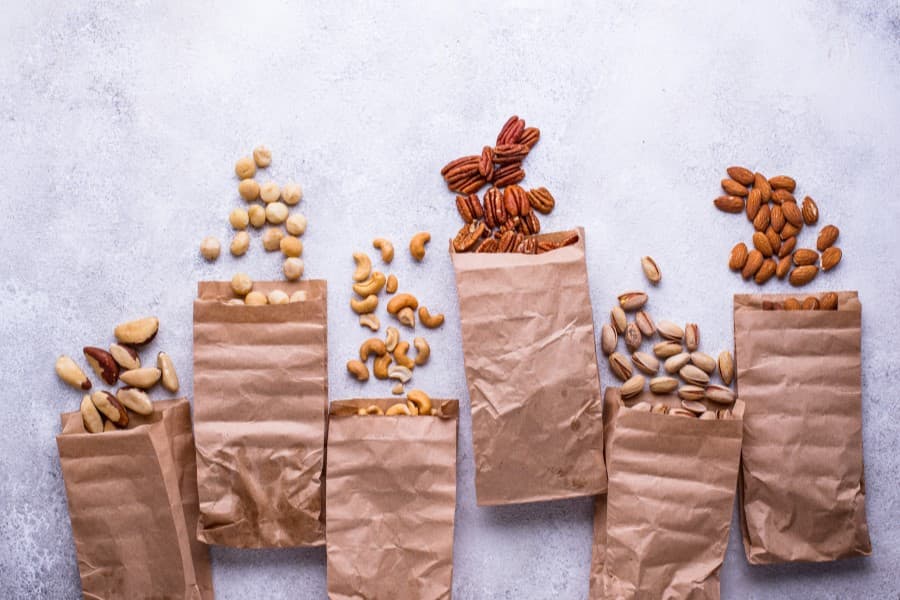 Różne rodzaje orzechów w papierowych torebkach, częściowo wysypane na blat.