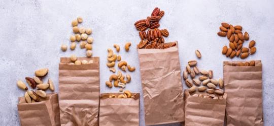 Różne rodzaje orzechów w papierowych torebkach, częściowo wysypane na blat.