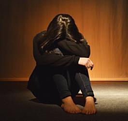 Kobieta siedzi na podłodze, głowę i ręce opiera o zgięte kolana.