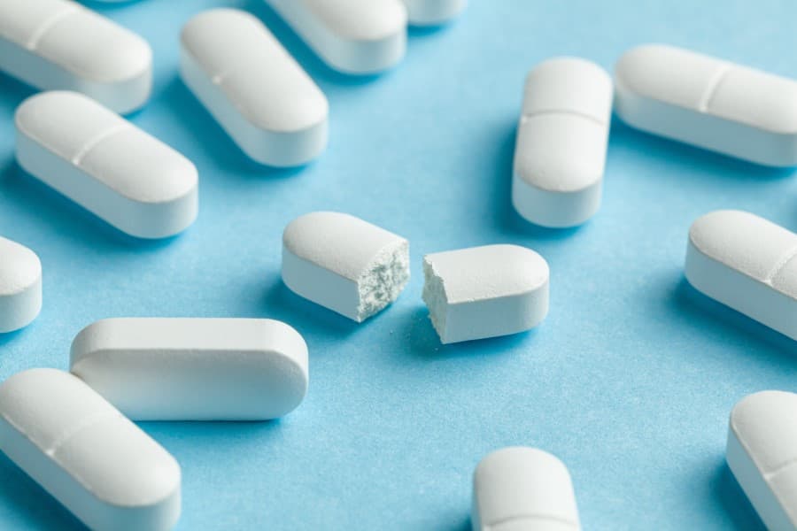 Białe tabletki z paracetamolem na niebieskim tle.