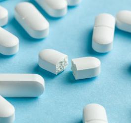 Białe tabletki z paracetamolem na niebieskim tle.