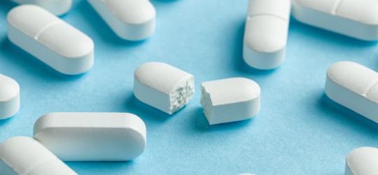 Białe tabletki z paracetamolem na niebieskim tle.