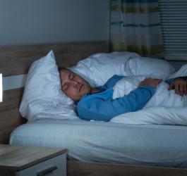 Mężczyzna w niebieskiej piżamie, śpi w swoim łóżku.