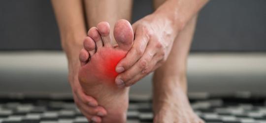 Mężczyzna odczuwa ból w stawie stopy z powodu podagry.