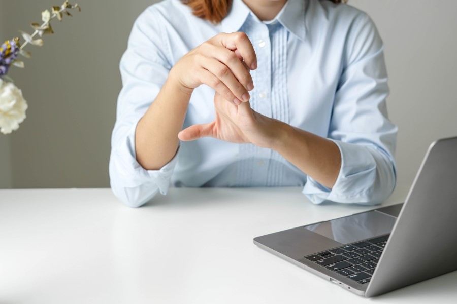 Kobieta siedzi przy biurku, zmaga się z objawami neuropatii w obrębie dłoni.