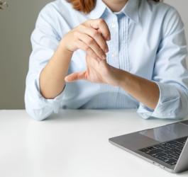 Kobieta siedzi przy biurku, zmaga się z objawami neuropatii w obrębie dłoni.