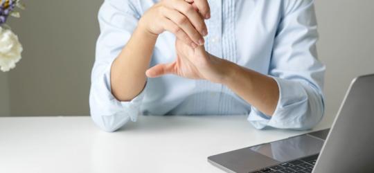 Kobieta siedzi przy biurku, zmaga się z objawami neuropatii w obrębie dłoni.